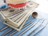 Dental artificial jaw instrument and one hundred dollar bills on dentist desk. Dental treatment cost concept