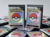 High-quality professional photograph of ultra rare sealed Pokémon card packs with a holographic card partially visible, on a clean white background